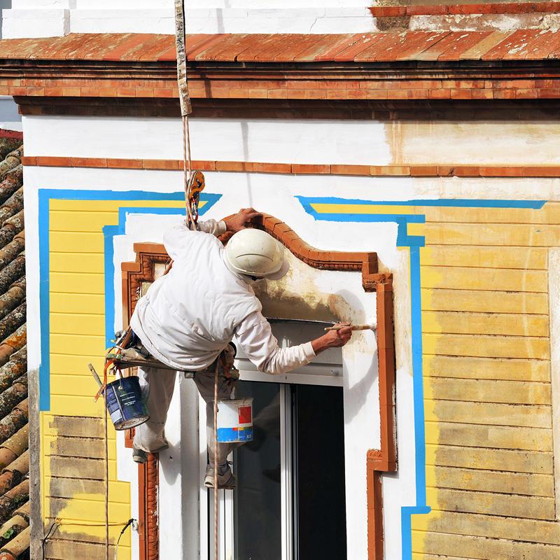 Man hanging from roof painting building
